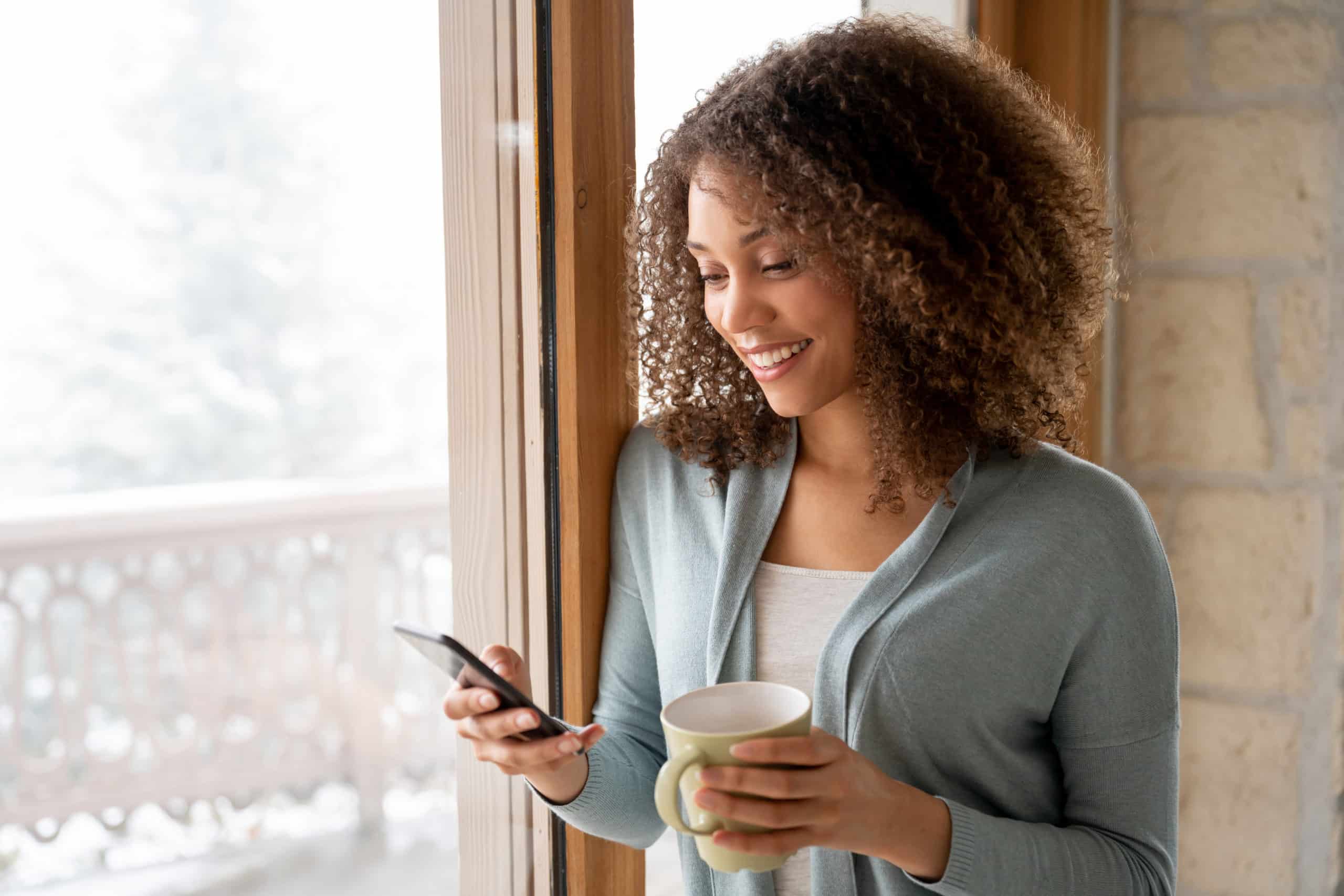Beautiful-woman-at-home-drinking-a-cup-of-coffee-and-texting-on-her-phone-scaled.jpg