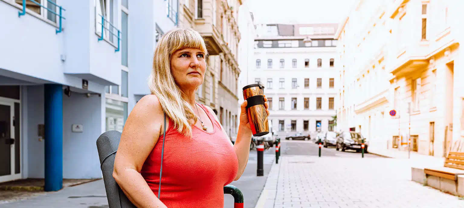 Mature happy middle aged woman 40s, long blond hair, smiling, big breasts, in jeans, holding yoga mat, thermos in hands